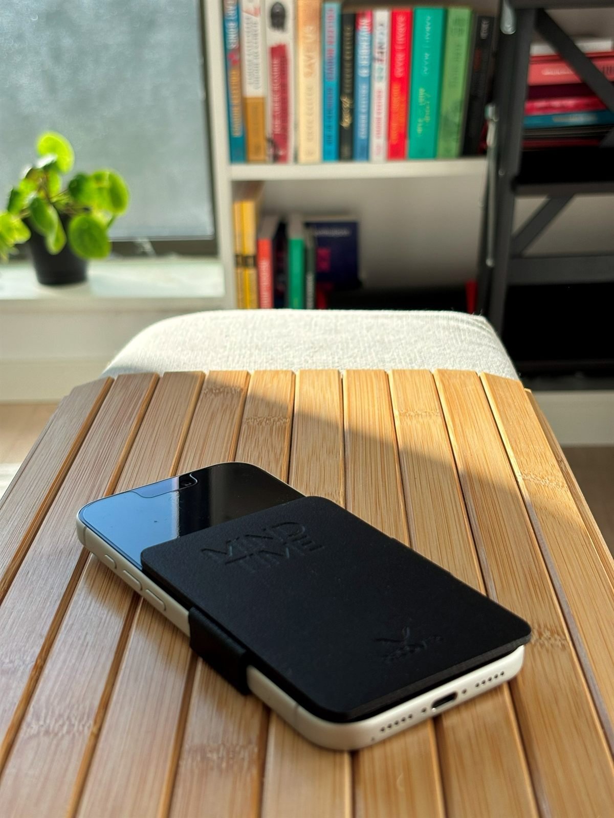 A phone with ReCover resting on a wooden armrest in late-afternoon sun, bookshelves softly out of focus behind.